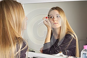 Reflection of young beautiful woman applying her make-up