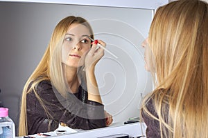 Reflection of young beautiful woman applying her make-up