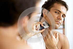 Reflection of young man in mirror shaving with electric shaver