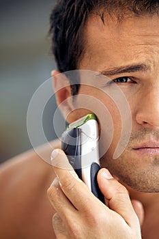 Reflection of young man in mirror shaving with electric shaver