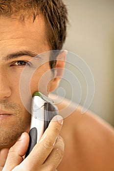 Reflection of young man in mirror shaving with electric shaver