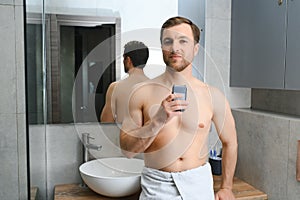 Reflection of young man in mirror shaving with electric shaver