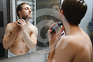 Reflection of young man in mirror shaving with electric shaver