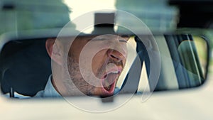 Reflection of young man in the rearview mirror, riding in a car and yawning. Right hand drive car. Lifestyle, travel