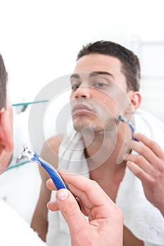 Reflection of young man shaving in bathroom mirror