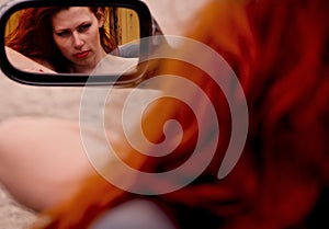 Reflection of a young redhead woman with wild red hair in the car mirror