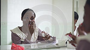 Reflection of young slim African American woman applying face moisturizer in slow motion. Portrait of beautiful young