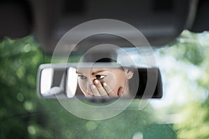 Reflection of young woman with crying eyes covering her face with hands in the car rear view mirror. Concept of an accident