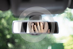 Reflection of young woman with frightened eyes covering her face with  hands in the car rear view mirror. Concept of an accident o