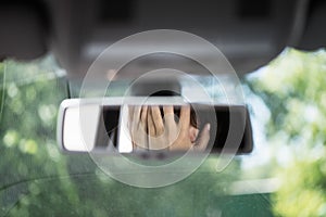 Reflection of young woman with frightened eyes covering her face with  hands in the car rear view mirror.