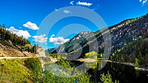 Reflections of blue sky, trees and mountains in the smooth surface on the crystal clear water of Crown Lake