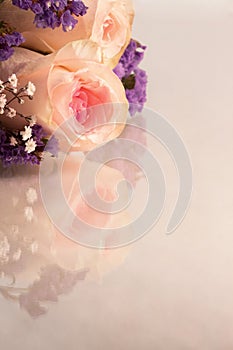 Pink roses and small lavender and white flowers on a reflective background with copy space