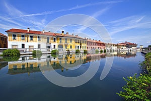 REFLECTIONS OF COLORFUL BUILDINGS ON THE WATER OF THE RIVER NAVIGLIO IN GAGGIANO VILLAGE IN ITALY