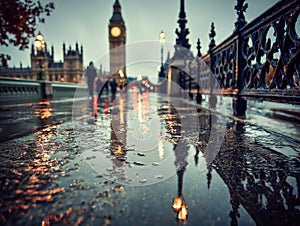 Reflections of an illuminated clock tower and historic architecture cast on a wet pedestrian bridge during twilight with blurred