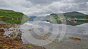 Reflections of the Portree Bay with a colorful seashore in the foreground and Ben Tianavaig mountain in the background, Isle of Sk