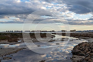 Reflections of sky in rocky tidal pools with the hotels of La Manga del Mar Menor in the background