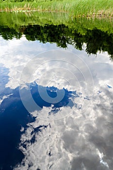 Reflections of tranquil blue sky with white clouds on water IV