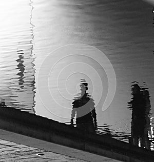 Reflections of two people on the rippled surface of a canal in t