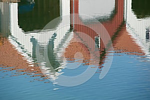 Reflections of white and red boat houses in water..