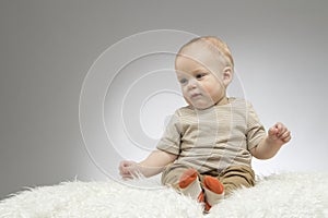 Reflective cute boy sitting on the white blanket, studio shot, isolated on grey background, funny baby portrait