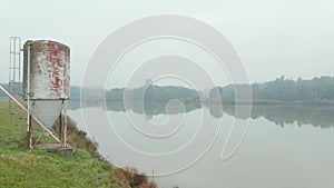 Reflective misty lake on an early autumn morning with a large metal silo, aerial