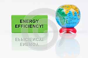On a reflective surface is a globe and a green sign with the inscription - Energy Efficiency