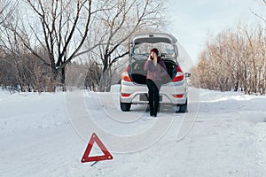 Reflective warning triangle before vehicle, an emergency situation on the road in winter, calls for help, woman talking