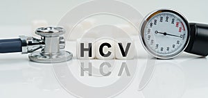 On a reflective white surface lies a stethoscope and cubes with the inscription - HCV