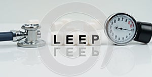 On a reflective white surface lies a stethoscope and cubes with the inscription - LEEP