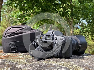 reflex camera with a bag on a stone against the background of green trees, concept of travel photography