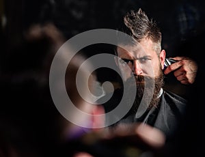 Reflexion of barbers hand with hair clipper trimming nape of client. Hipster bearded client getting hairstyle in front