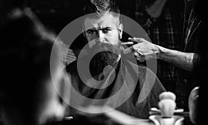 Reflexion of barbers hand with hair clipper trimming nape of client. Hipster bearded client getting hairstyle in front
