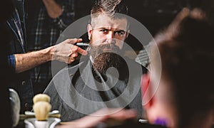 Reflexion of barbers hand with hair clipper trimming nape of client. Hipster bearded client getting hairstyle in front