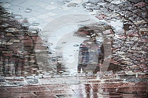 Reflexion of couple with umbrella on cobbles place