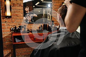 Reflexion of a hairdresser making a haircut for a young man in a barber shop