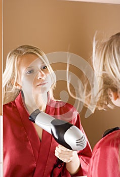 Reflexion of young blone woman using hair drier photo