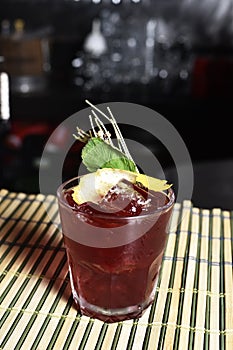 Refreshing alcoholic drink with berries, ice vodka and gin, lemon peel served in glass cup on the counter on black background