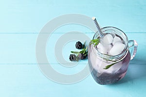 Refreshing blackberry drink with rosemary and ice cubes in mason jar on turquoise wooden table. Space for text