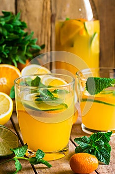 Refreshing citrus lemonade with fresh mint, glasses, bottle, cut fruits on wood kitchen table