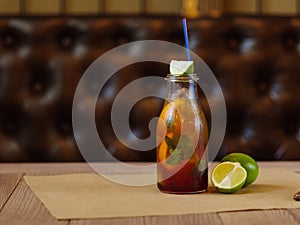 A refreshing cocktail with slices of lemon, green lime and leaves of mint on a blurred wooden background.