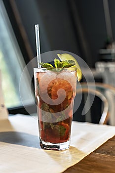 Refreshing cocktail with a straw on the table by the window in the cafe