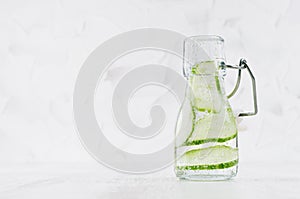 Refreshing cold detox drink with green cucumber, bright bubbles in transparent yoke bottle in elegant white interior on wood table