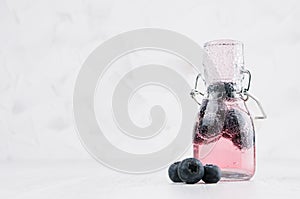 Refreshing cold fruit pink drink with blueberry, bright bubbles in transparent yoke bottle in elegant white interior on wood table