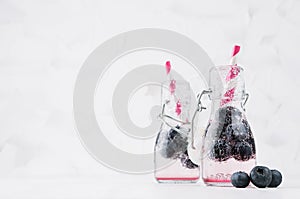 Refreshing cold fruit pink drinks with blueberry, bright bubbles and straw in transparent yoke bottles in elegant white interior.