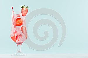 Refreshing cold strawberry beverage with red fruit slices, ice cubes, sparkling water, striped straw in misted glass in mint color