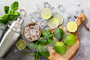 Refreshing cold summer Mojito cocktail making. Mint, lime, ice ingredients and bar utensils on a stone or concrete table.