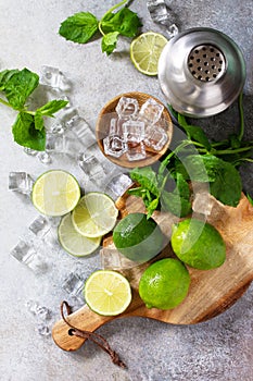 Refreshing cold summer Mojito cocktail making. Mint, lime, ice ingredients and bar utensils on a stone or concrete table.