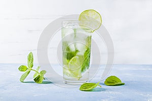 Refreshing cool detox drink with lime and mint on blue background. Summer lemonade or ice tea in a glass. Mojito cocktail with ice