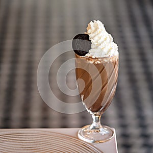 Refreshing drink. Glass of chocolate milkshake cocktail with Airy foam or froth and cookie on top. Puffy whipped cream