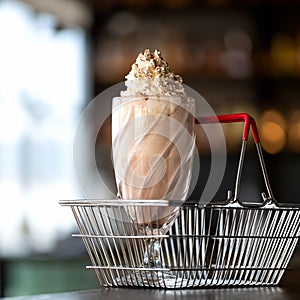 Refreshing drink. Glass of milkshake cocktail in grocery shopping basket. Side view of Cold cream dessert or smoothie on